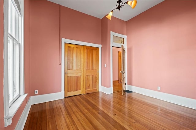 unfurnished bedroom featuring an inviting chandelier, baseboards, and hardwood / wood-style floors