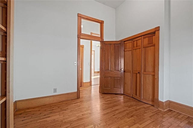 interior space featuring a closet, baseboards, light wood-style floors, and a towering ceiling