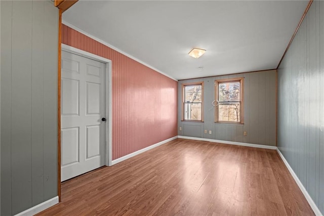 empty room featuring crown molding, wood finished floors, and baseboards