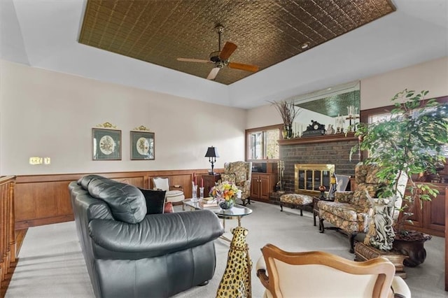 living area featuring light colored carpet, a ceiling fan, a brick fireplace, and a tray ceiling