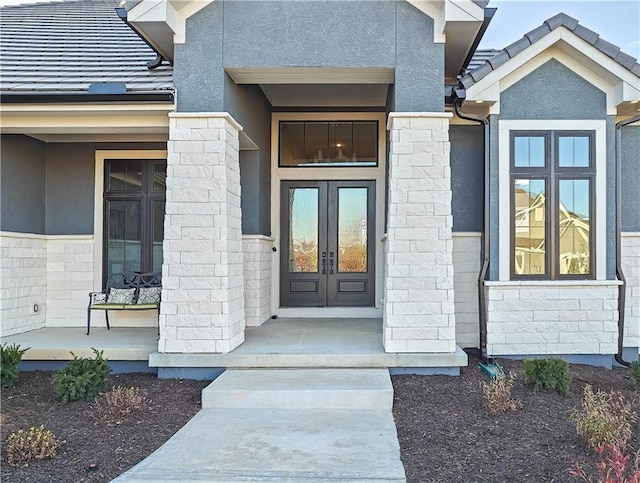 view of exterior entry with stone siding, stucco siding, french doors, and a tile roof