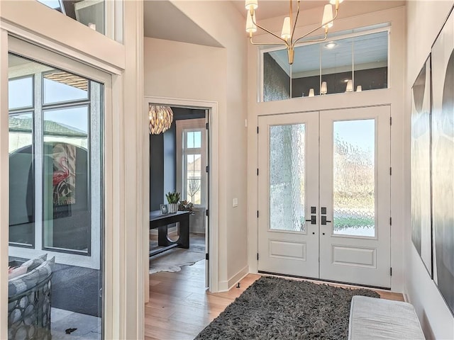 foyer entrance with a chandelier, french doors, baseboards, and light wood-style floors