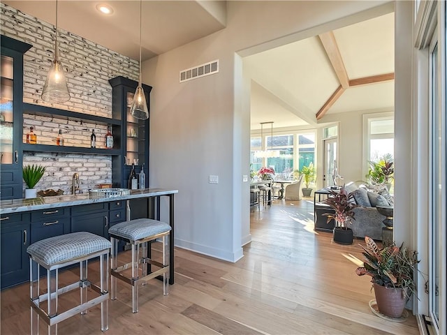 bar featuring light wood-type flooring, visible vents, decorative light fixtures, baseboards, and wet bar