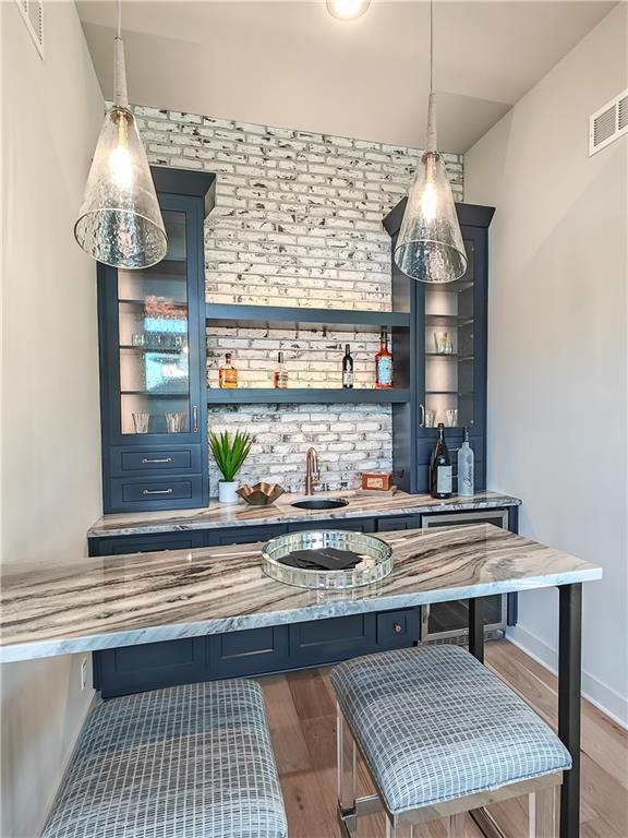 bar with visible vents, a sink, decorative light fixtures, wood finished floors, and indoor wet bar