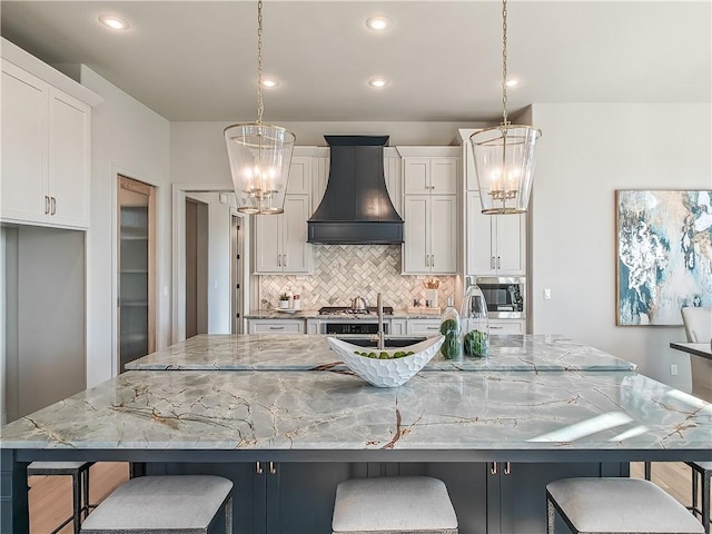 kitchen with decorative backsplash, custom exhaust hood, a large island with sink, and a chandelier