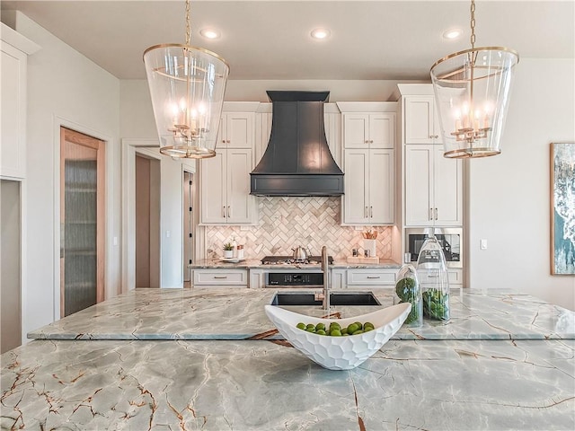 kitchen with premium range hood, light stone countertops, tasteful backsplash, and an inviting chandelier