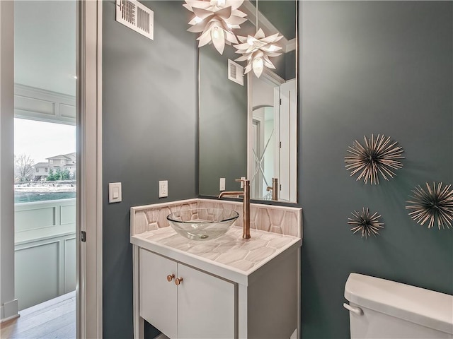 half bath with vanity, toilet, a ceiling fan, and visible vents