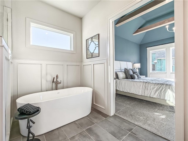 ensuite bathroom featuring wainscoting, ensuite bathroom, a freestanding tub, tile patterned floors, and a decorative wall