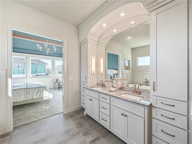 ensuite bathroom with double vanity, a chandelier, connected bathroom, and a sink