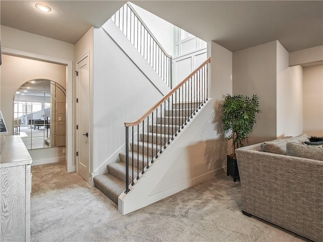 staircase featuring arched walkways, carpet flooring, and baseboards