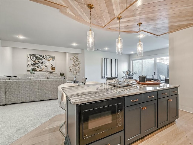 kitchen with light wood-type flooring, pendant lighting, open floor plan, a center island, and black microwave