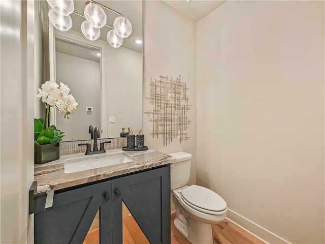 half bath featuring baseboards, toilet, wood finished floors, and vanity