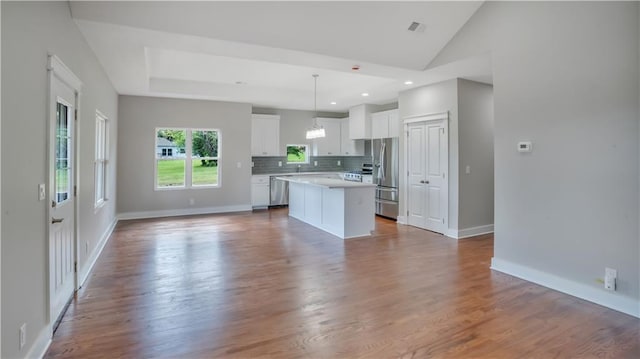 kitchen with appliances with stainless steel finishes, a kitchen island, white cabinetry, open floor plan, and decorative backsplash