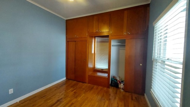 unfurnished bedroom featuring a closet, baseboards, wood finished floors, and crown molding