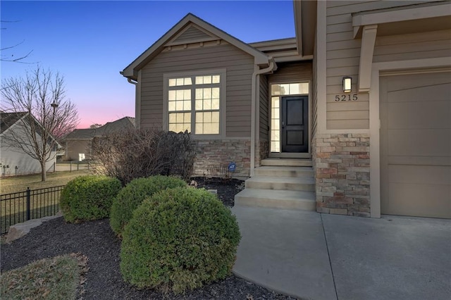 exterior entry at dusk featuring stone siding and fence