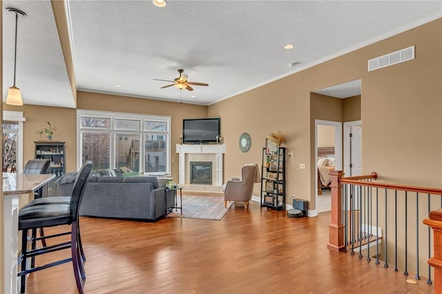 living area with wood finished floors, a ceiling fan, visible vents, a tile fireplace, and crown molding