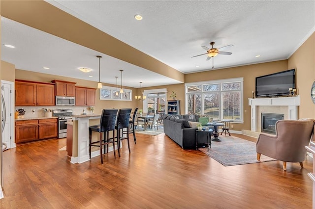 living area featuring a glass covered fireplace, recessed lighting, wood finished floors, and ceiling fan