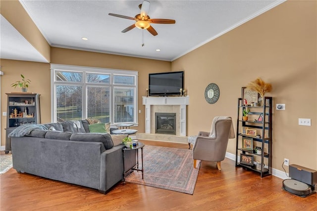 living room featuring wood finished floors, crown molding, a ceiling fan, and a high end fireplace