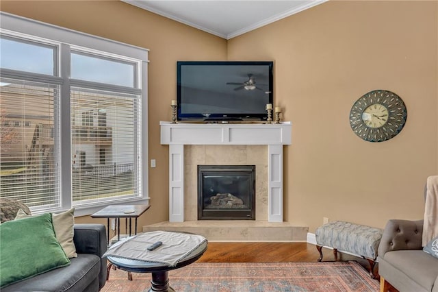 living room with a ceiling fan, wood finished floors, baseboards, a fireplace, and ornamental molding