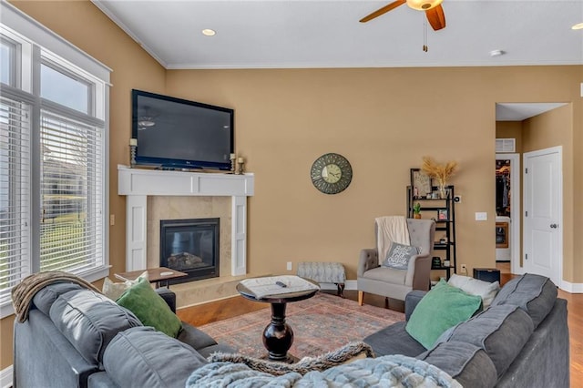 living room featuring wood finished floors, baseboards, a fireplace, ceiling fan, and crown molding