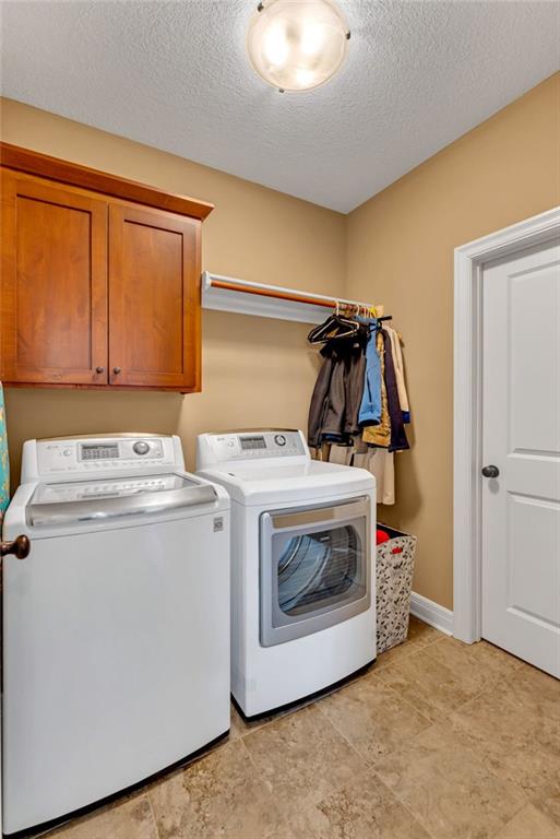 washroom with washing machine and clothes dryer, cabinet space, a textured ceiling, and baseboards