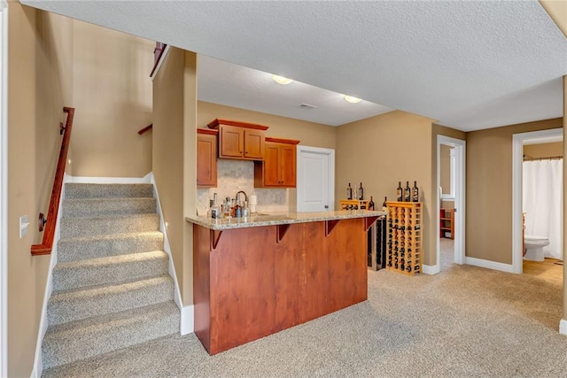 kitchen with a breakfast bar area, light stone countertops, a peninsula, light colored carpet, and brown cabinets