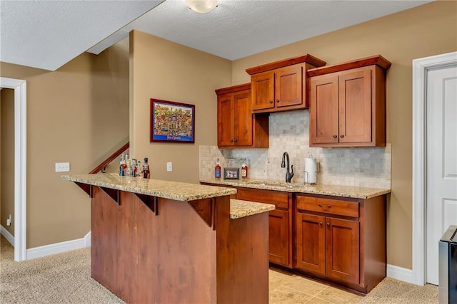 kitchen featuring a sink, decorative backsplash, a breakfast bar, and brown cabinetry