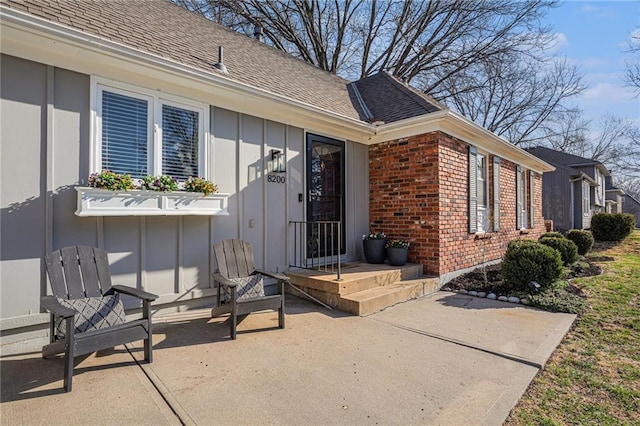 exterior space featuring a patio area, brick siding, and roof with shingles