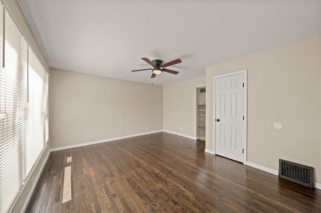 empty room with dark wood-type flooring, a ceiling fan, visible vents, and baseboards