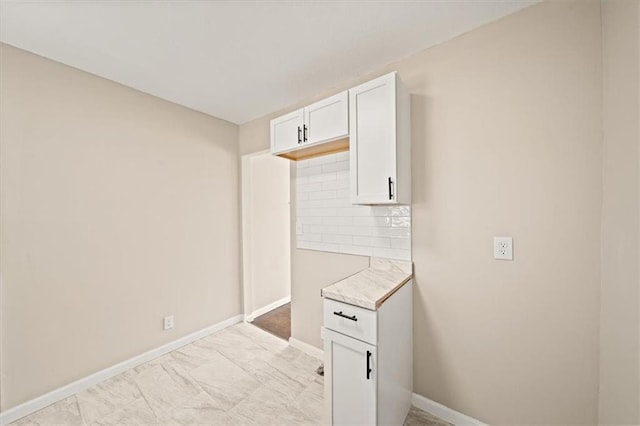 kitchen with white cabinetry, light countertops, baseboards, and backsplash