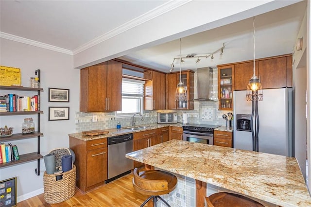 kitchen featuring brown cabinetry, ornamental molding, a sink, appliances with stainless steel finishes, and wall chimney range hood