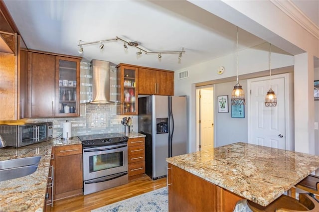 kitchen with visible vents, stainless steel appliances, light wood-style floors, brown cabinetry, and wall chimney range hood