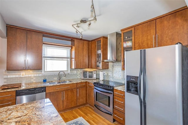 kitchen featuring a sink, stainless steel appliances, light wood-style floors, wall chimney exhaust hood, and brown cabinetry