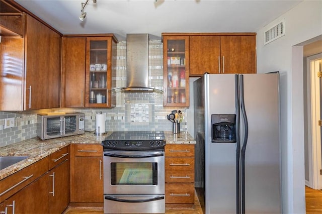 kitchen featuring light stone counters, visible vents, stainless steel appliances, and wall chimney range hood