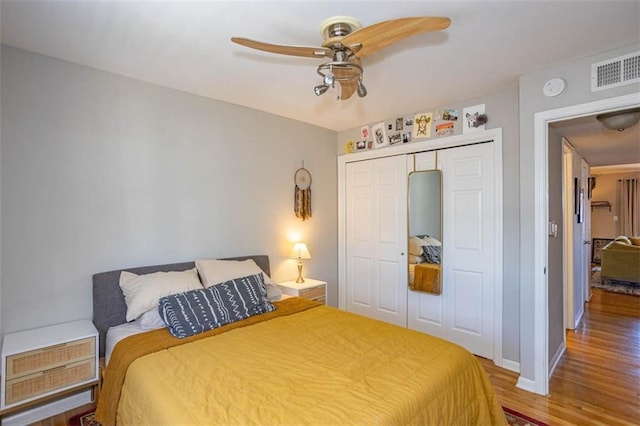 bedroom with a ceiling fan, wood finished floors, visible vents, baseboards, and a closet