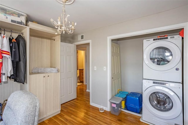 laundry area featuring stacked washer / dryer, visible vents, a chandelier, light wood-type flooring, and laundry area