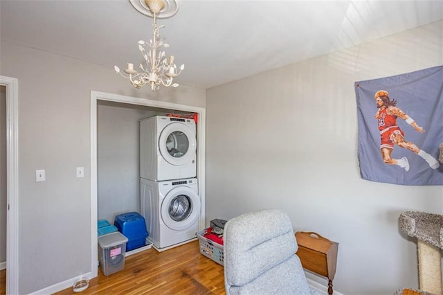 laundry room with wood finished floors, stacked washer / dryer, baseboards, a chandelier, and laundry area