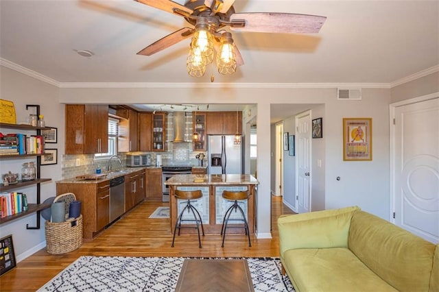 kitchen with visible vents, a sink, stainless steel appliances, wall chimney exhaust hood, and brown cabinetry