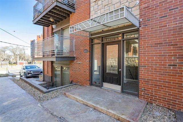 entrance to property with brick siding, a balcony, and fence