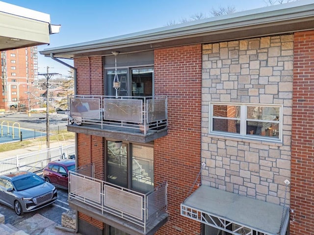 back of house with a balcony, fence, and brick siding