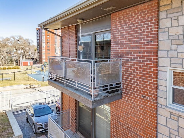 view of home's exterior featuring brick siding, a balcony, and fence