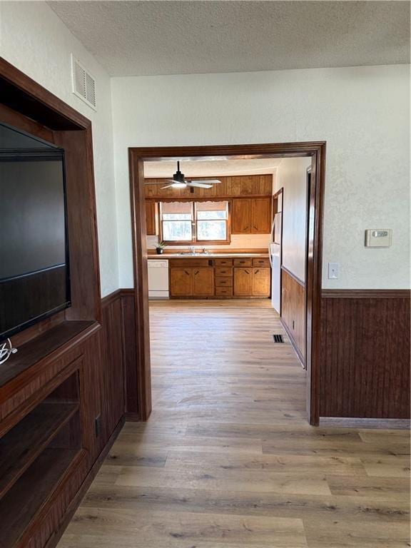 hallway featuring visible vents, a textured ceiling, wood walls, wainscoting, and light wood finished floors