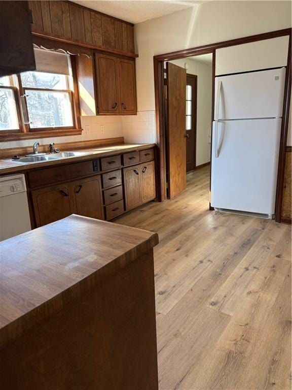 kitchen with a sink, white appliances, tasteful backsplash, and light wood finished floors