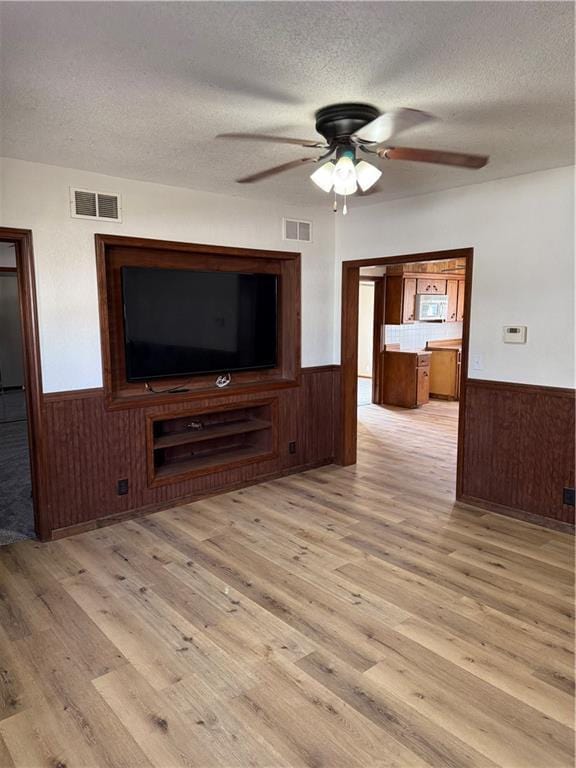 unfurnished living room with a wainscoted wall, visible vents, and ceiling fan