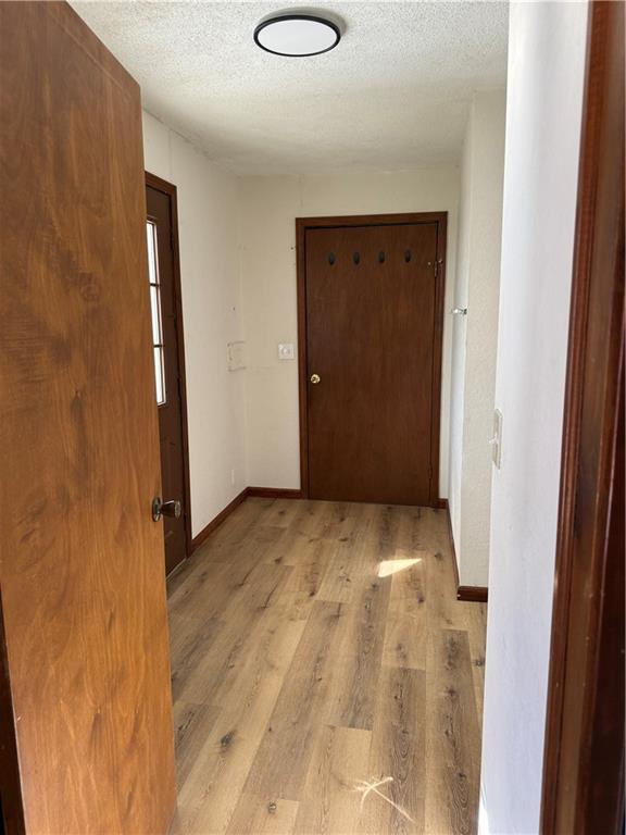 corridor with a textured ceiling, light wood-type flooring, and baseboards