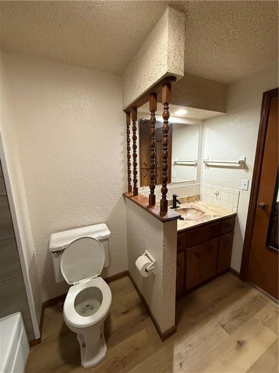 bathroom with a textured ceiling, toilet, a textured wall, and wood finished floors