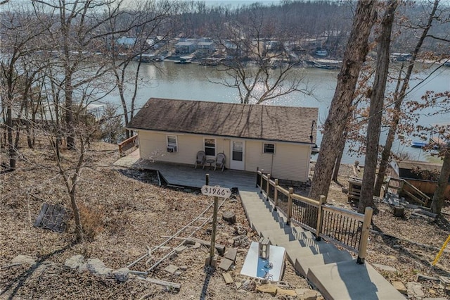 rear view of house featuring a shingled roof, a deck with water view, and fence