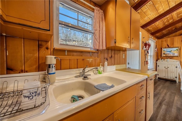 kitchen with wooden walls, light countertops, lofted ceiling with beams, wooden ceiling, and a sink