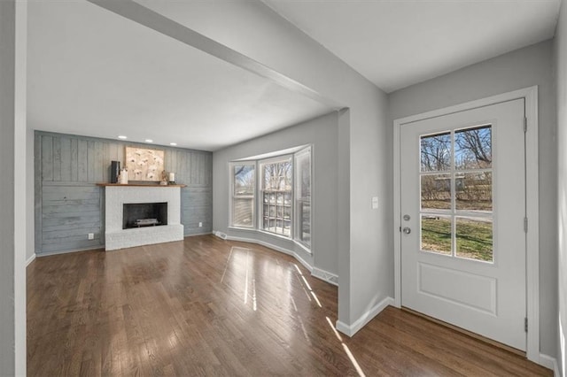 foyer entrance featuring dark wood-style floors, plenty of natural light, a fireplace, and baseboards