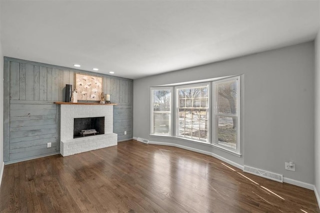 unfurnished living room with wood finished floors, visible vents, baseboards, recessed lighting, and a brick fireplace